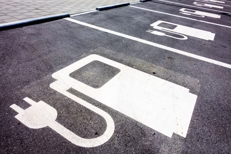 Close-up of white electric car charging symbol on black pavement in parking spaces.